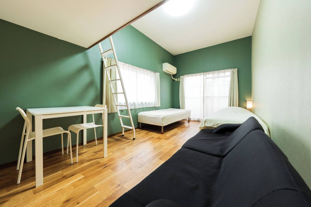 A room with a loft bed, a desk with chairs, a ladder, and a window with curtains.
