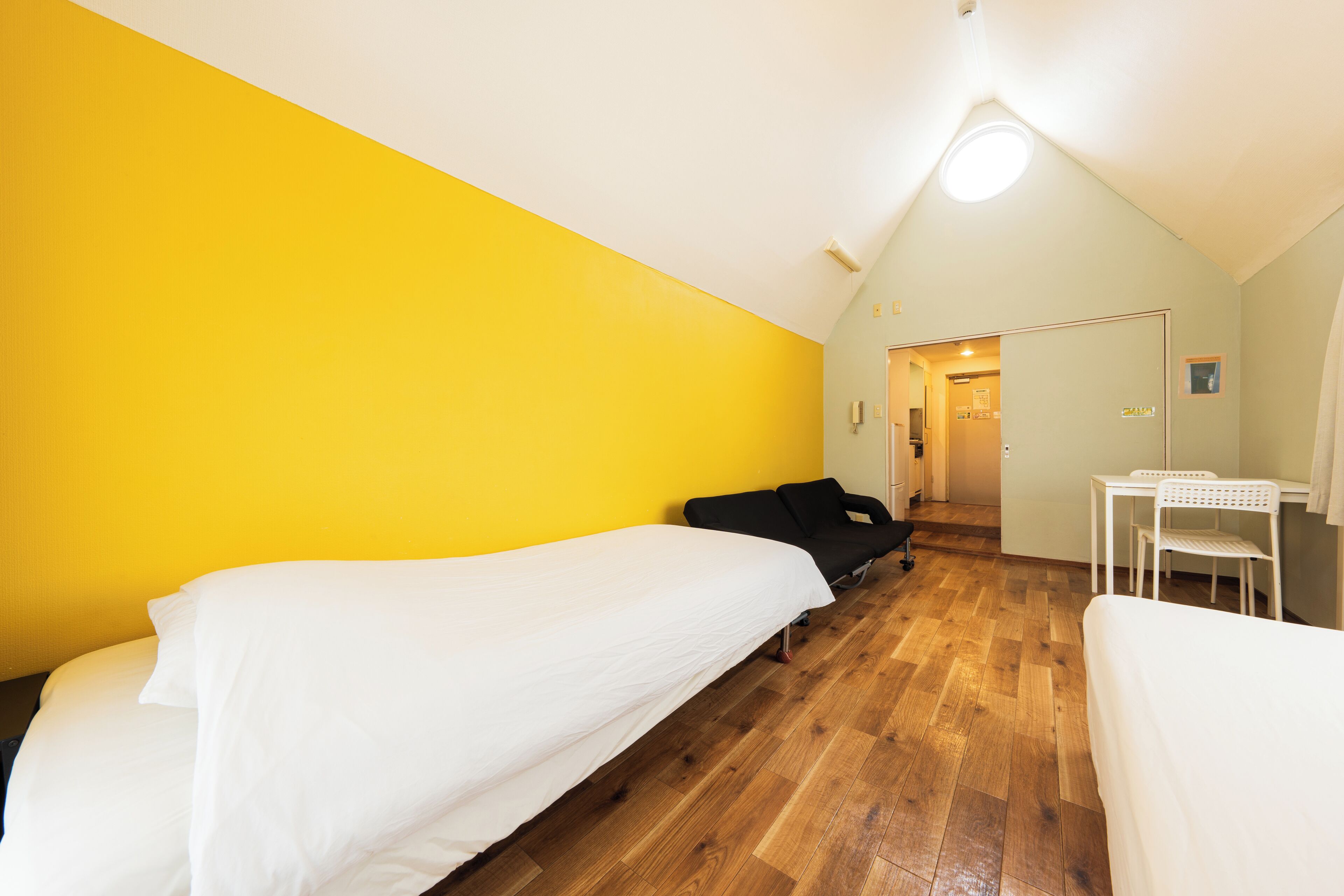 Una habitación con dos camas individuales, piso de madera, pared amarilla y techo blanco.