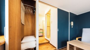 Een kamer met een houten garderobe, een bankje en een deur naar een andere kamer.