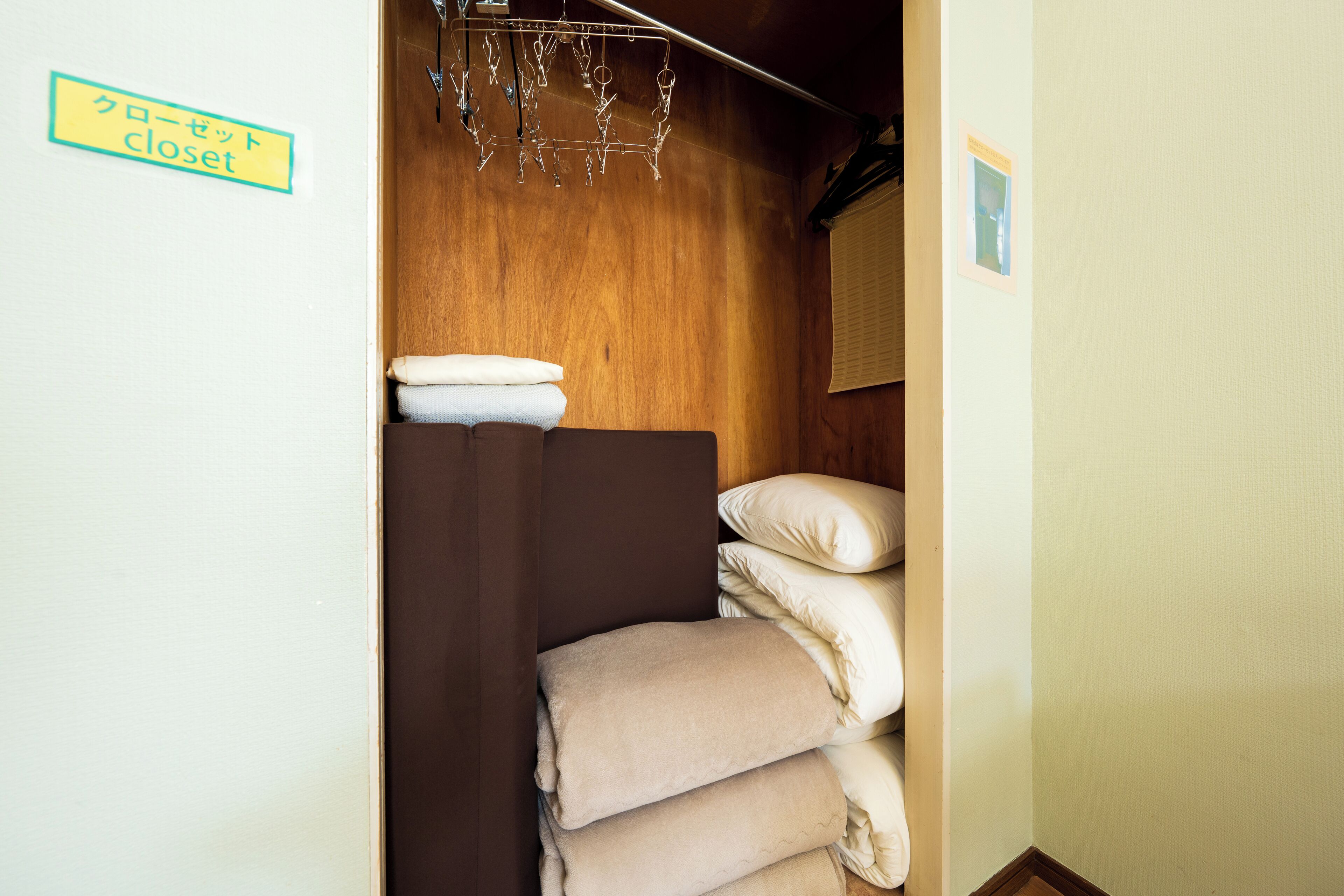 A closet with a sign indicating its location, a hanging rack with clothes, and neatly stacked towels.