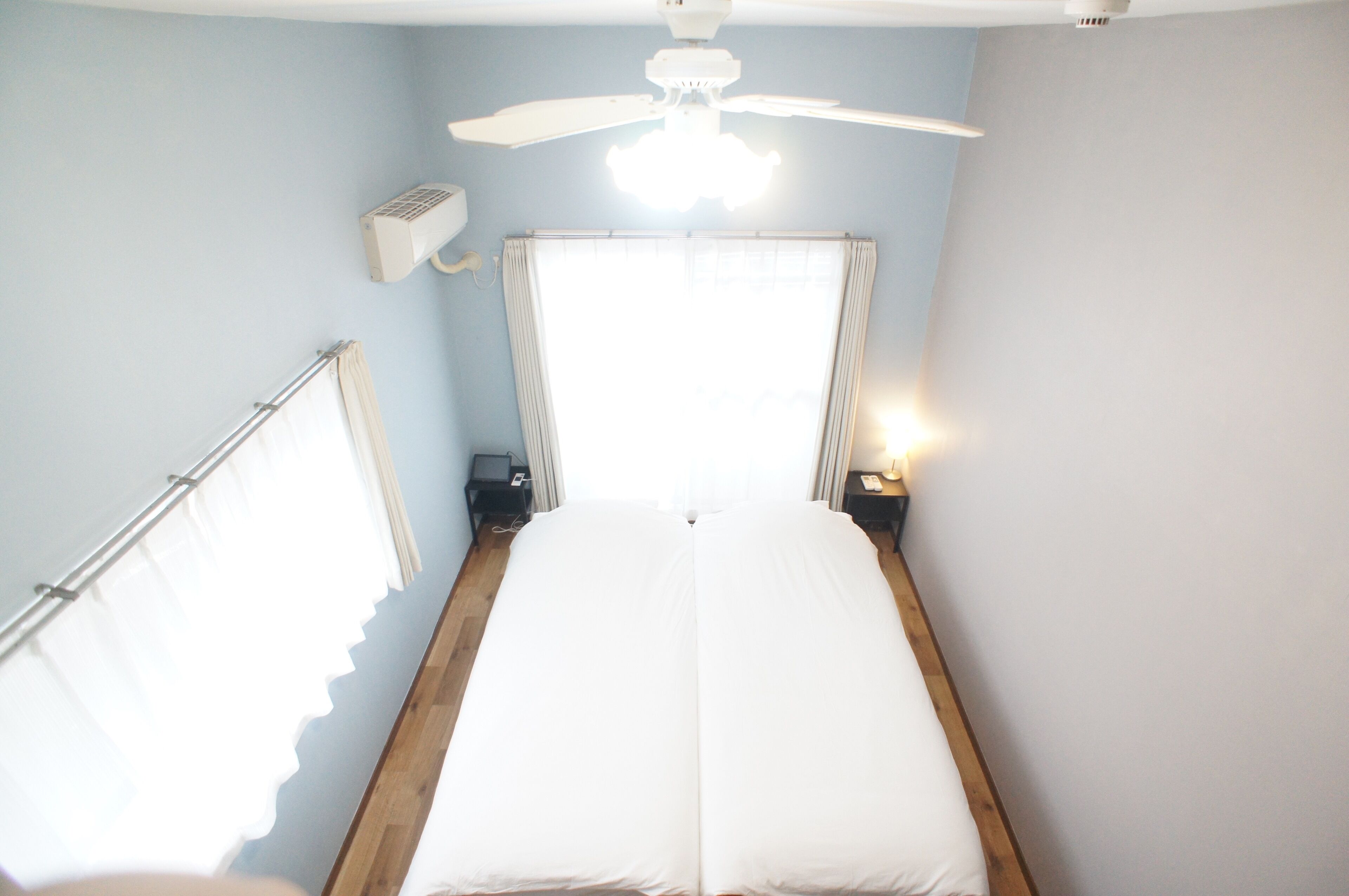 A room with a bed, a ceiling fan, a window with curtains, and a bedside table with a lamp.