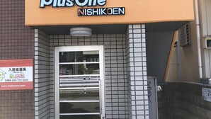 Entree van een PlusOne Nishikoen gebouw, met een betegelde gevel, een metalen poort en een bord.
