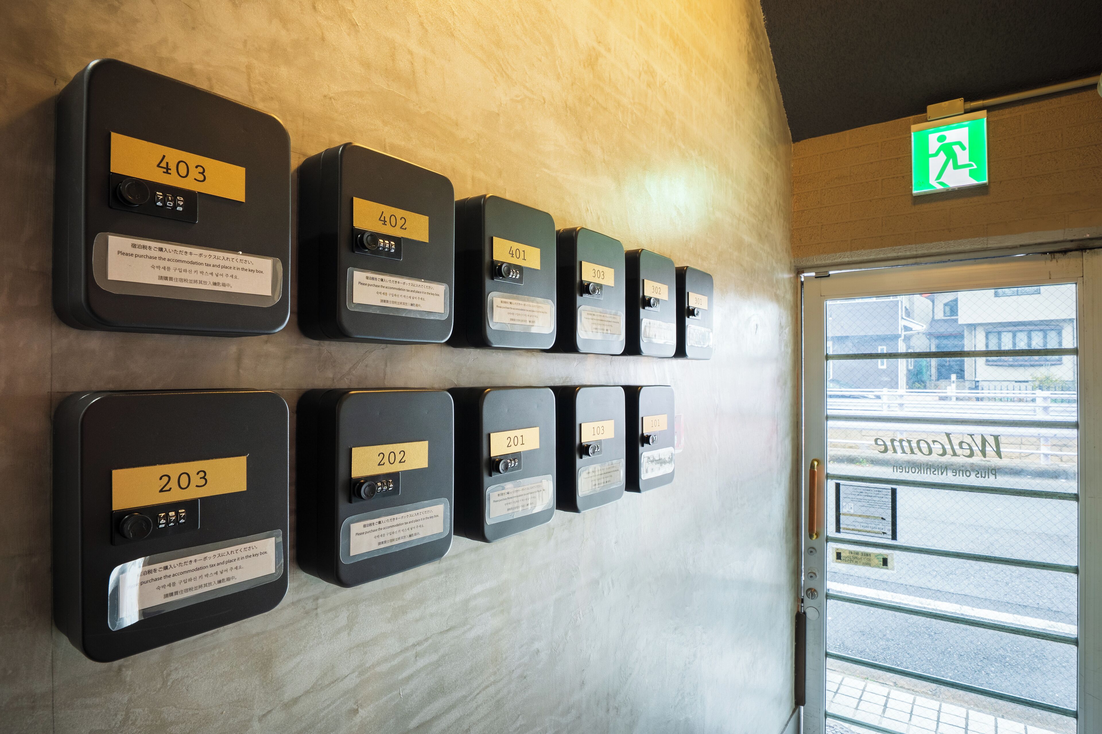 A wall with numbered room call buttons, a door with a window, and a green exit sign.