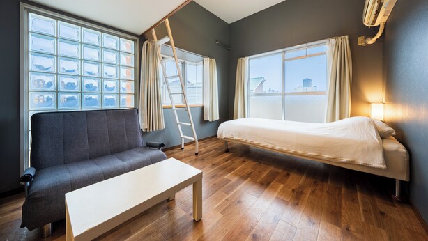 Een kamer met een bank, een bed, een tafel en een raam met gordijnen.