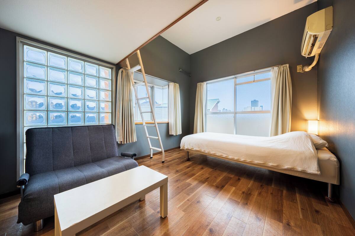 A room with a sofa, a bed, a table, and a window with curtains.