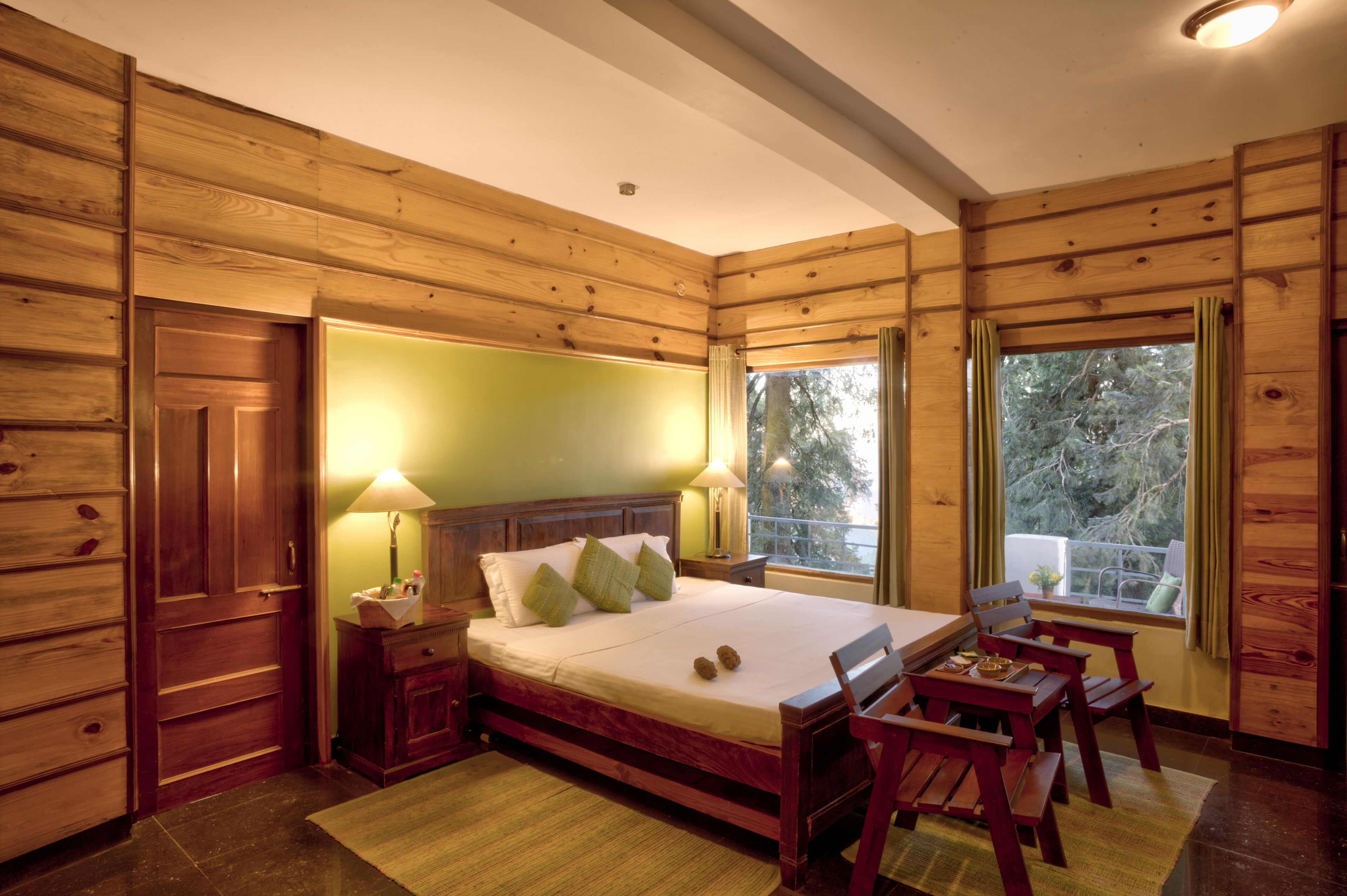 A wooden-paneled bedroom with a bed, bedside lamps, a window with curtains, and a view of trees.