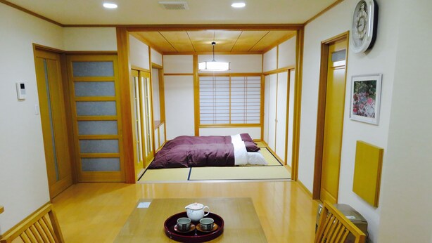 A traditional Japanese room with tatami flooring, a low bed, and a dining table with a tea set. - Utatei Villa (Takayama)