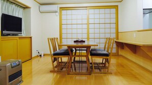 A room with a wooden dining table, four chairs, a television on a cabinet, an air conditioner, and a sliding door with a grid pattern. - Utatei Villa (Takayama)