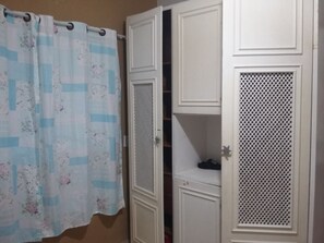 Features a spacious wardrobe with a louvered door and decorative panel, complemented by a stylish curtain.