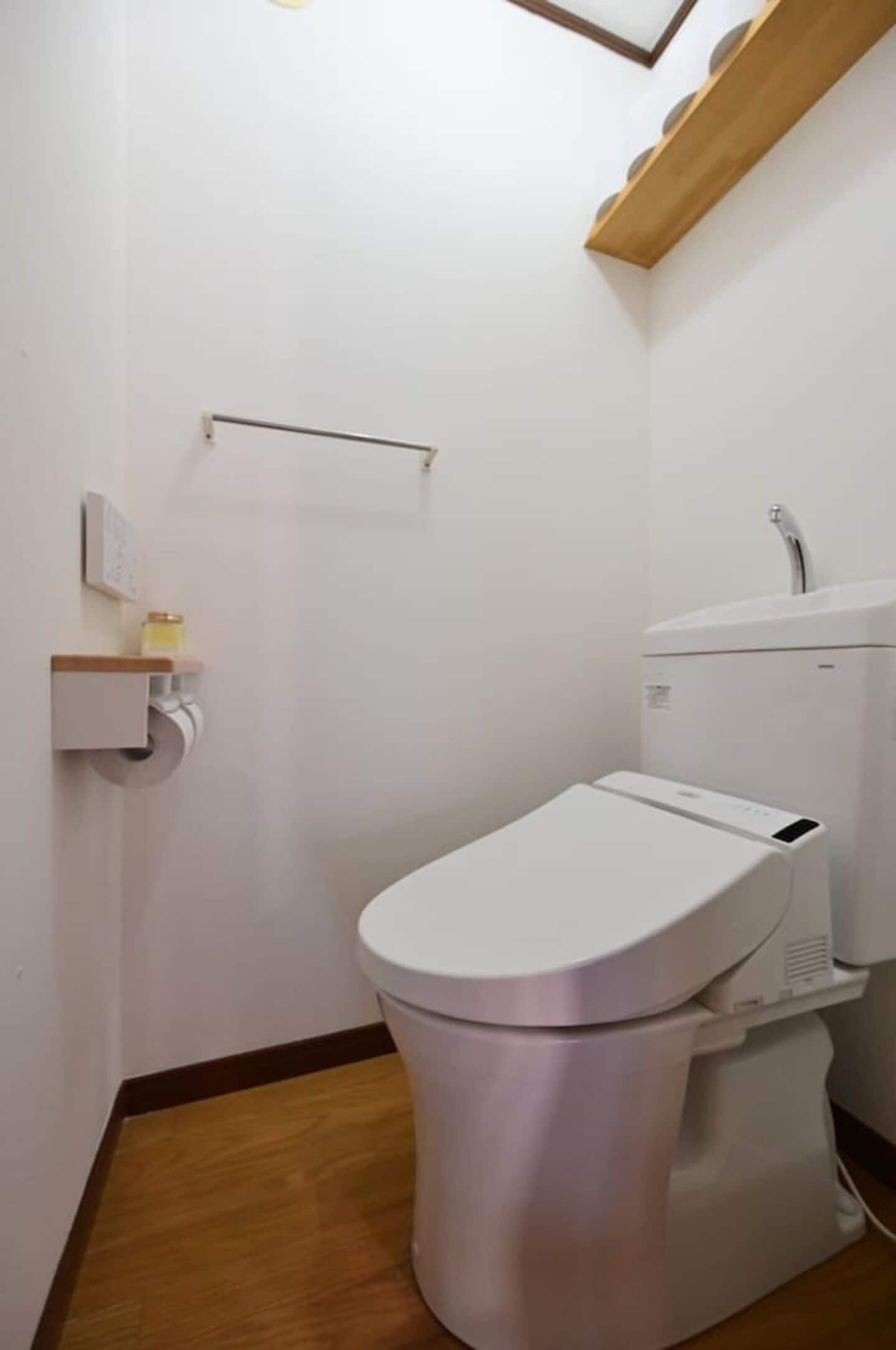 A small, modern bathroom with a white toilet, a wooden floor, and a white wall.