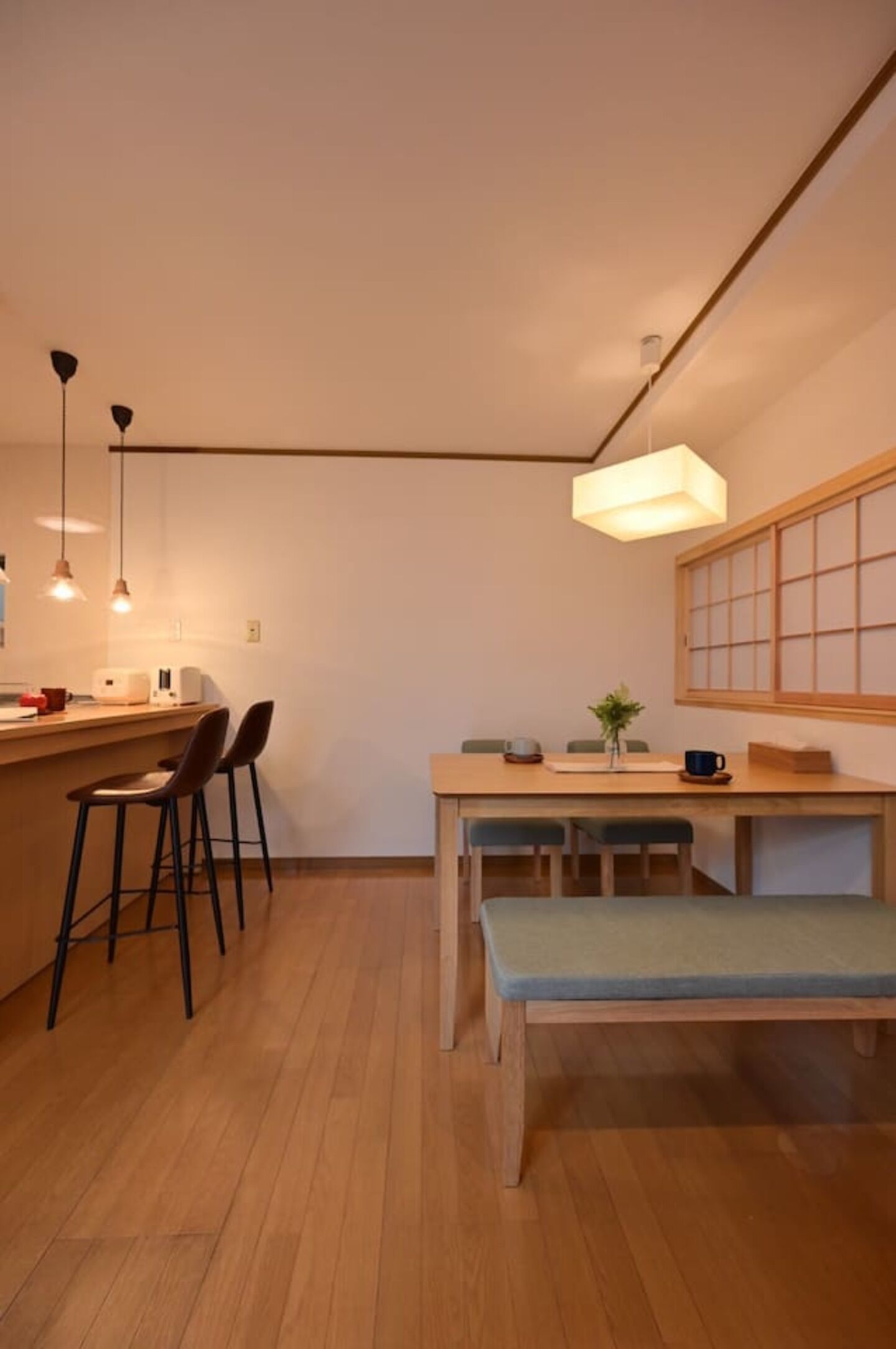 A compact kitchen with a wooden countertop, bar stools, a bench, and pendant lighting.