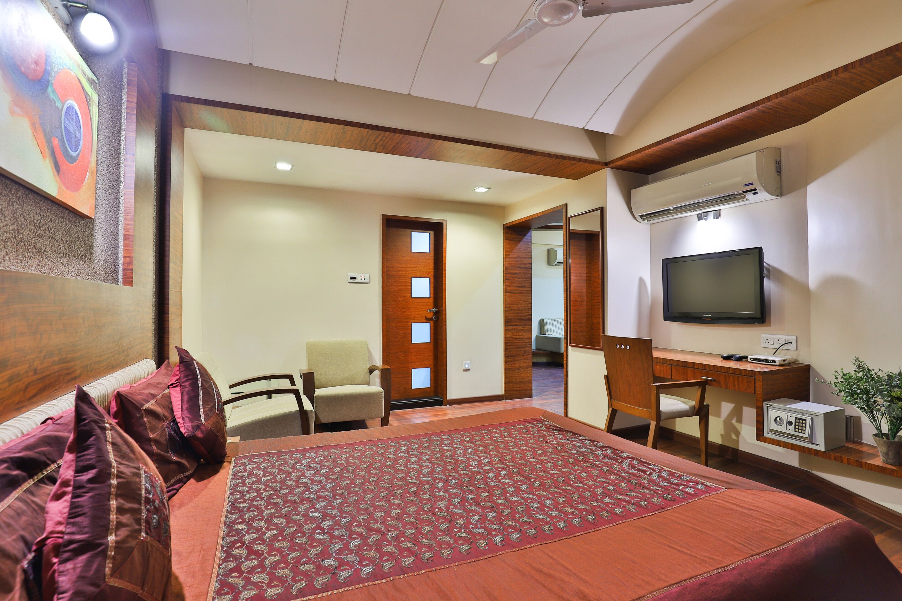 A hotel room with a bed, a desk, a television, and a small plant.