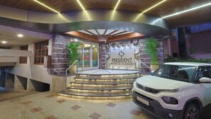 Entrada de un hotel con una escalera curva, un SUV blanco estacionado en la parte delantera y un letrero que dice "President Hotel & Banquet".