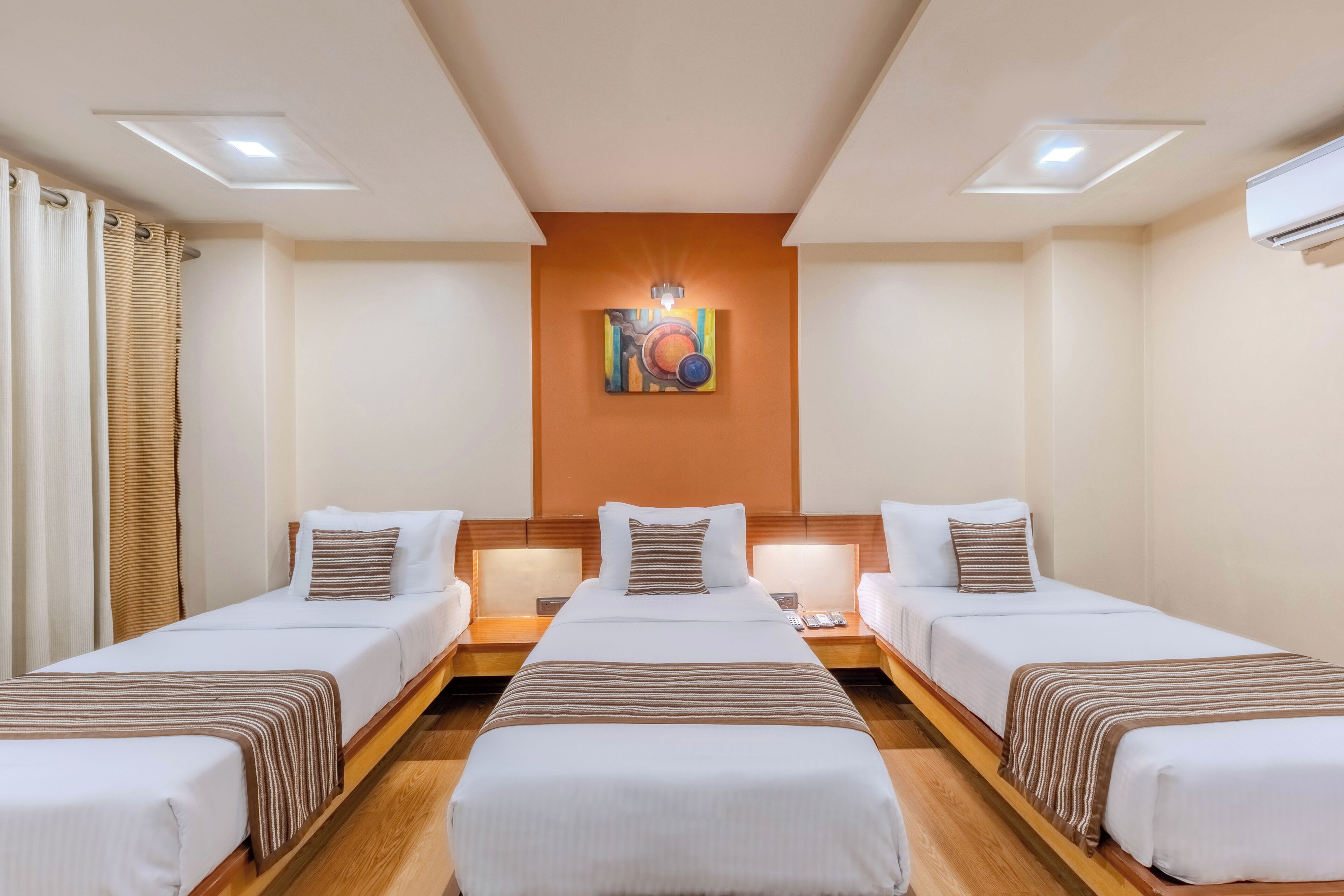 A hotel room with two single beds, a large bed, and a wall-mounted artwork.