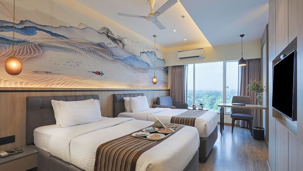 Habitación de hotel con dos camas, un escritorio, un televisor y un mural en la pared.