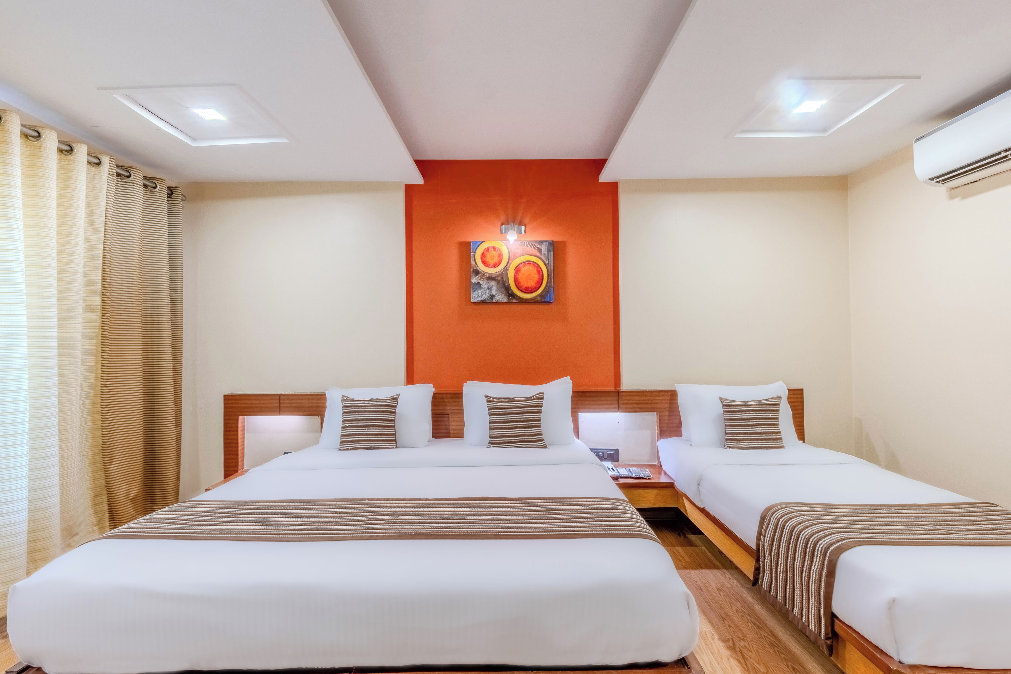 A hotel room with two single beds, a wooden headboard, a wall-mounted artwork, and a ceiling light.