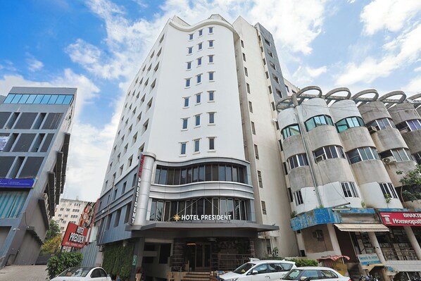 A multi-story hotel with a prominent 'HOTEL PRESIDENT' sign, a modern architectural design, and a parking area in front. - Hotel President (Vadodara)