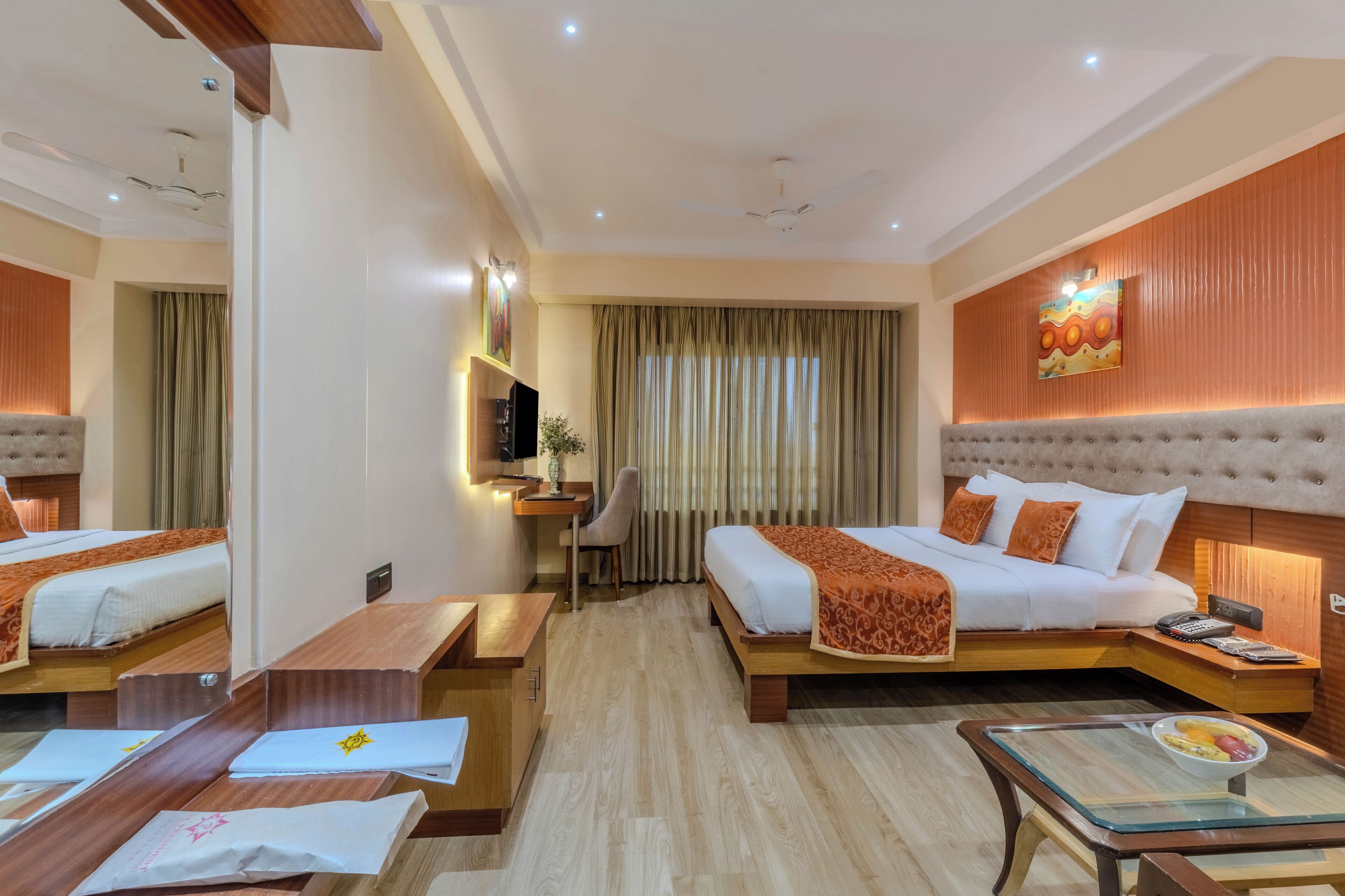 A hotel room with two beds, a desk, a chair, a small table, and a TV.