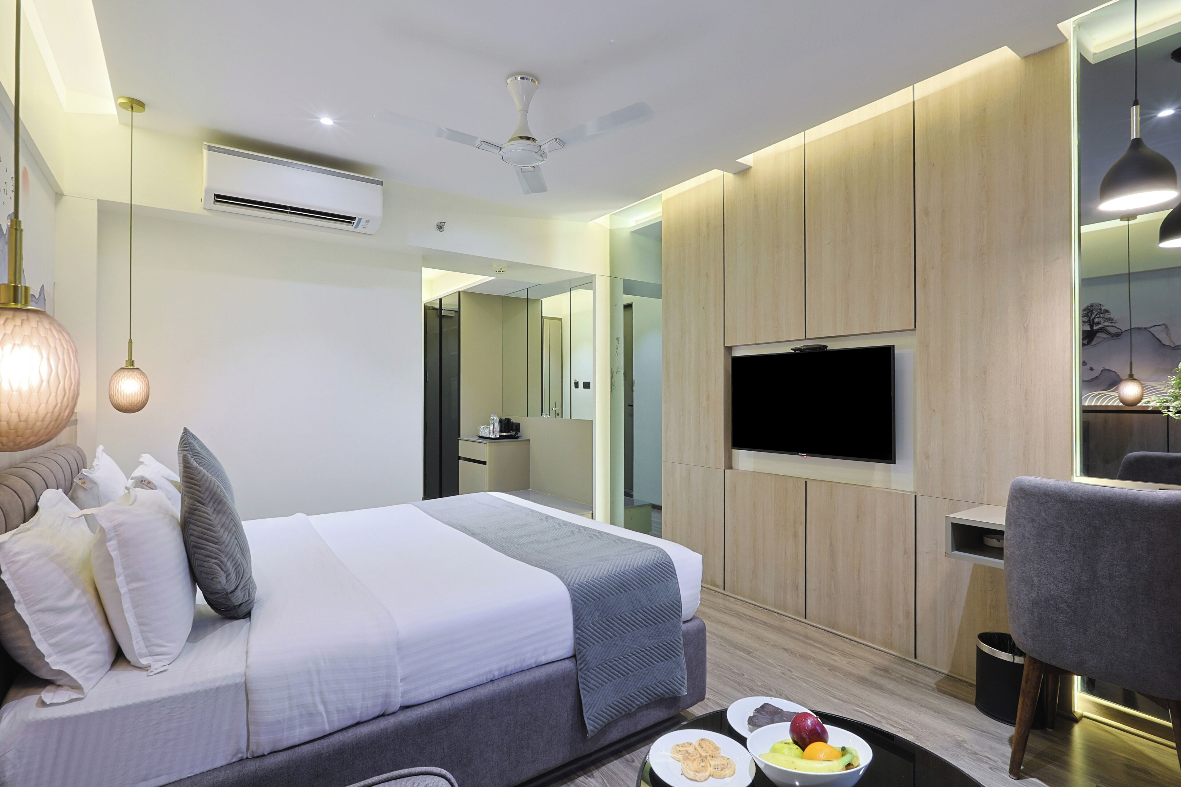 Een moderne hotelkamer met een bed, een bureau, een televisie en een zithoek met fruit.