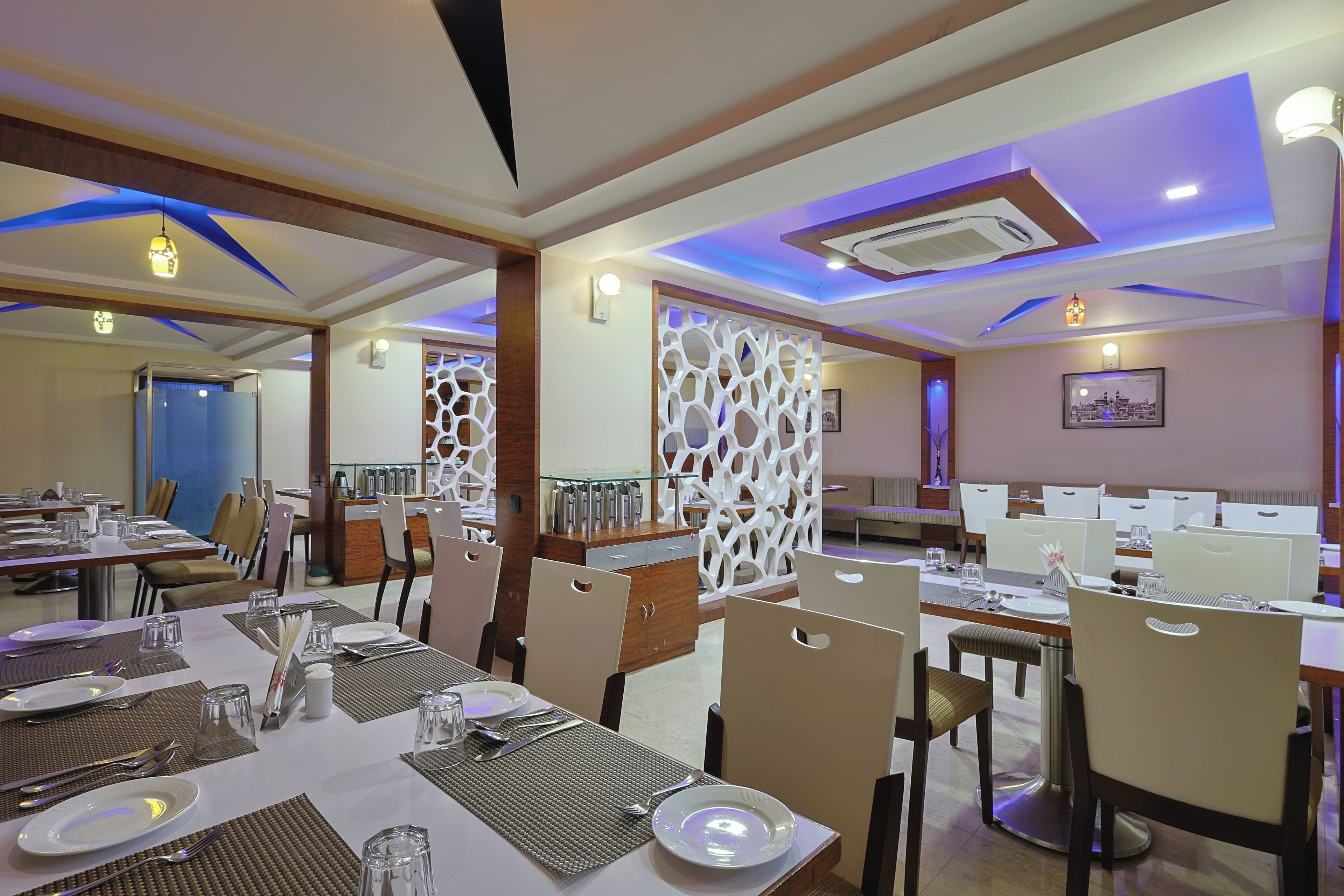 Comedor con mesas dispuestas para varios comensales, sillas y un panel blanco decorativo.