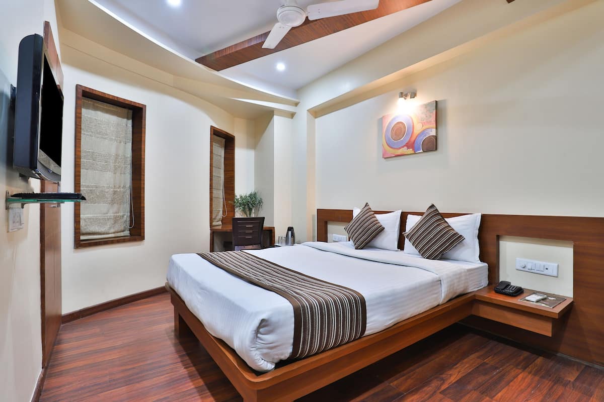 A hotel room with a large bed, a desk, a chair, a TV, and a ceiling fan.