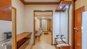 Habitación de hotel con piso de madera, un escritorio con silla, una mesita, un espejo y un armario.