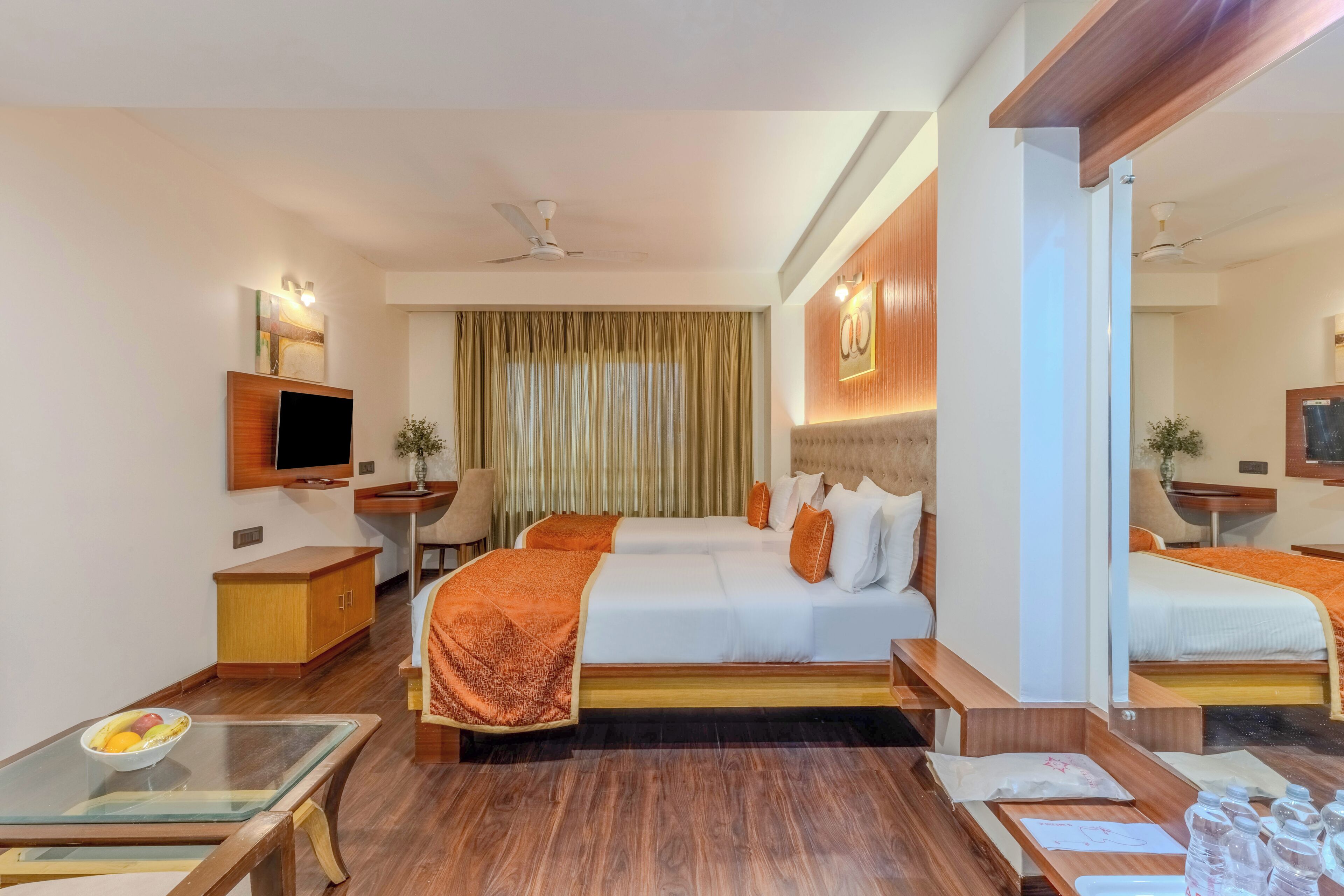 Habitación de hotel con dos camas, un televisor de pantalla plana, un armario de madera, una mesa de cristal y un ventilador de techo.