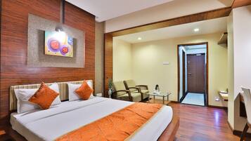 A hotel room with a large bed, a desk, a chair, and a door leading to another room.