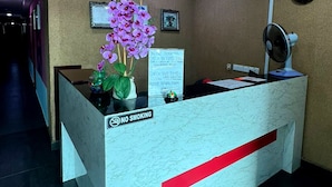 A reception desk with a 'No Smoking' sign, a clock, and a vase of purple flowers. - De Glory Hotel USJ 21 (Subang Jaya)