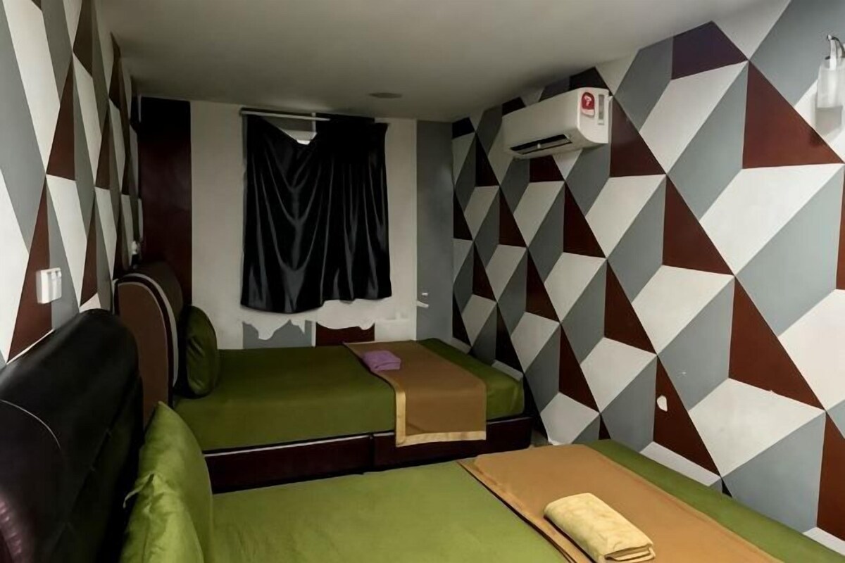 A room with two beds, a couch, a window with curtains, and a geometric-patterned wall.