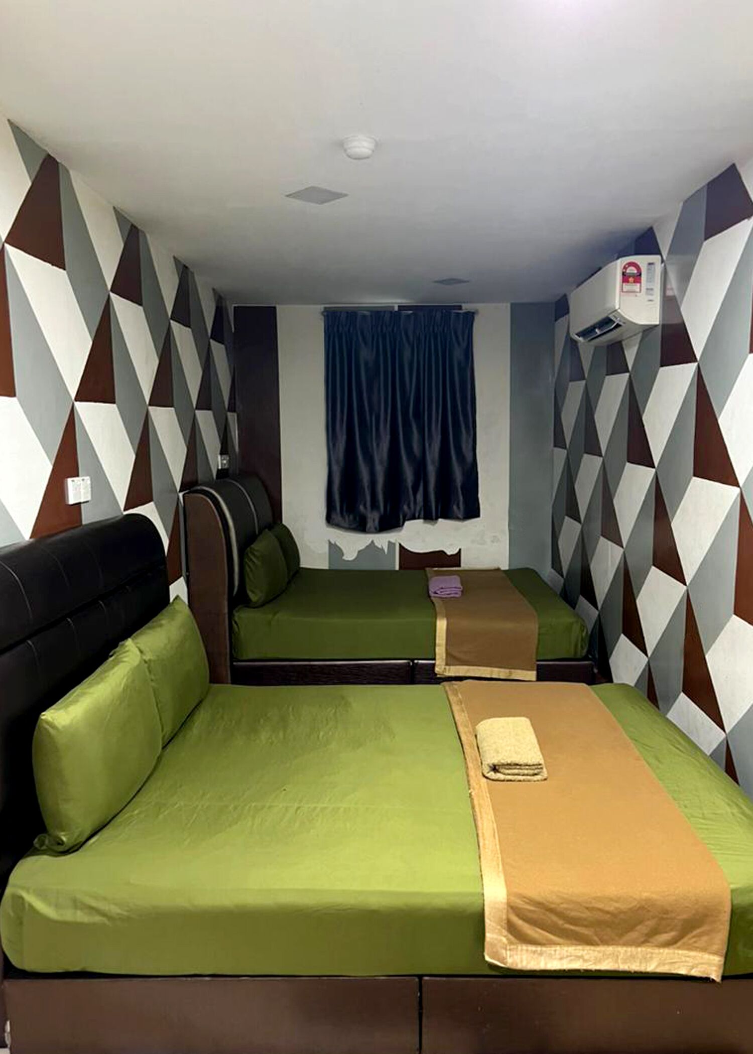 Een kamer met twee bedden, een blauw gordijn, een plafondlamp en een luchtverkoeler aan de muur.