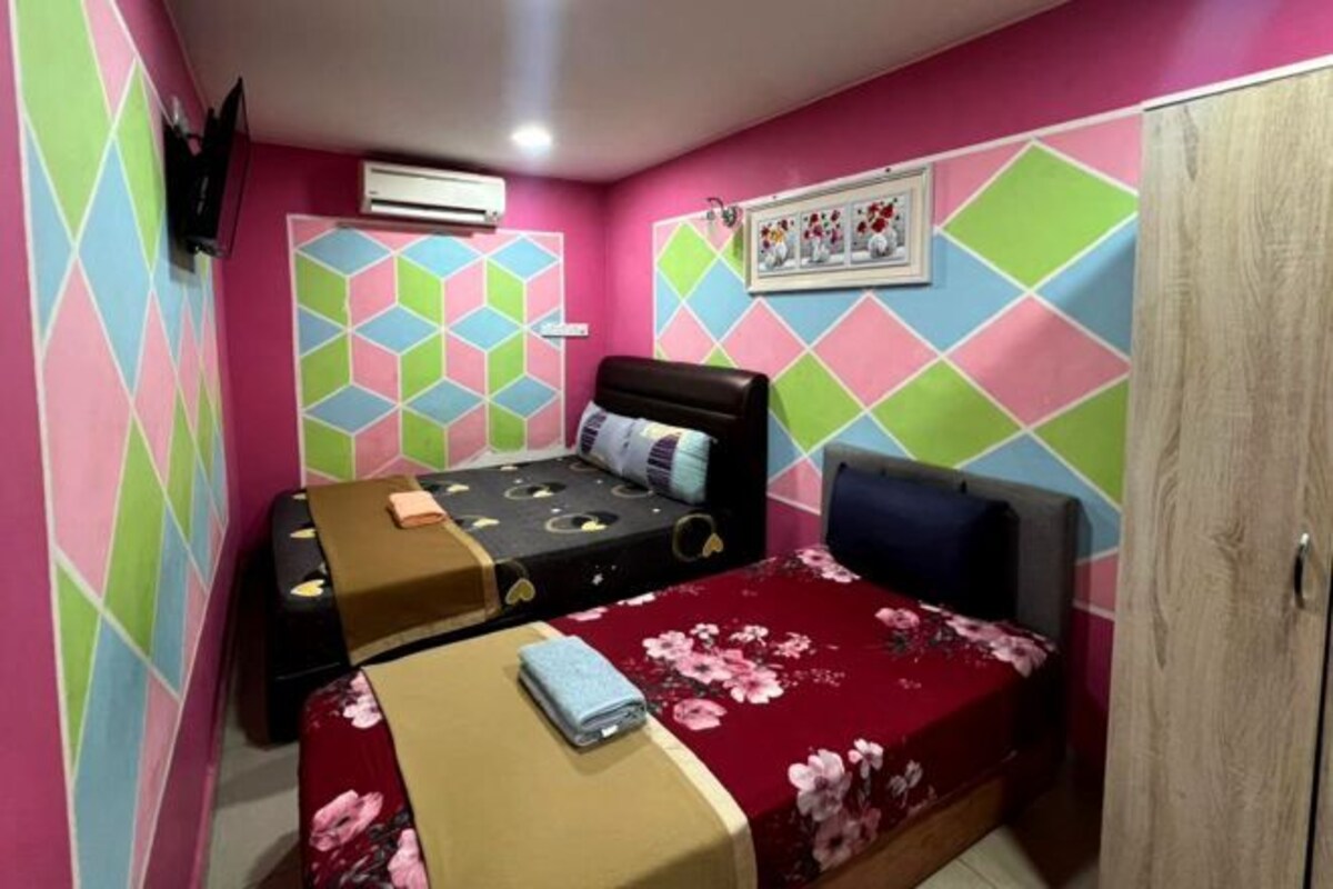 A small, colorful room with two beds, a wooden wardrobe, and a wall-mounted air conditioner.