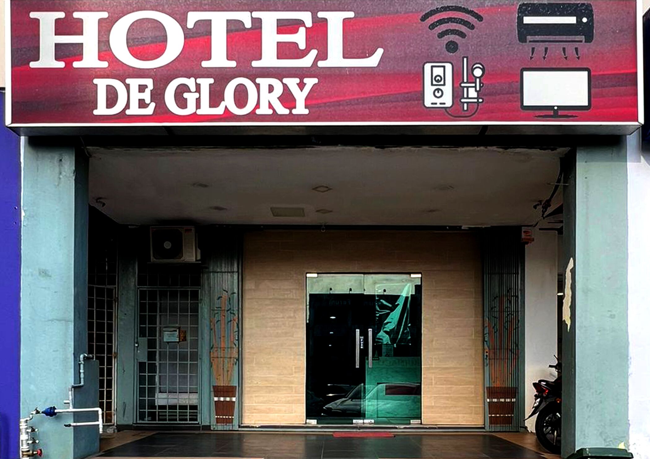 Entrada de un hotel con un letrero que dice "HOTEL DE GLORY", una cámara de seguridad y un símbolo de Wi-Fi.