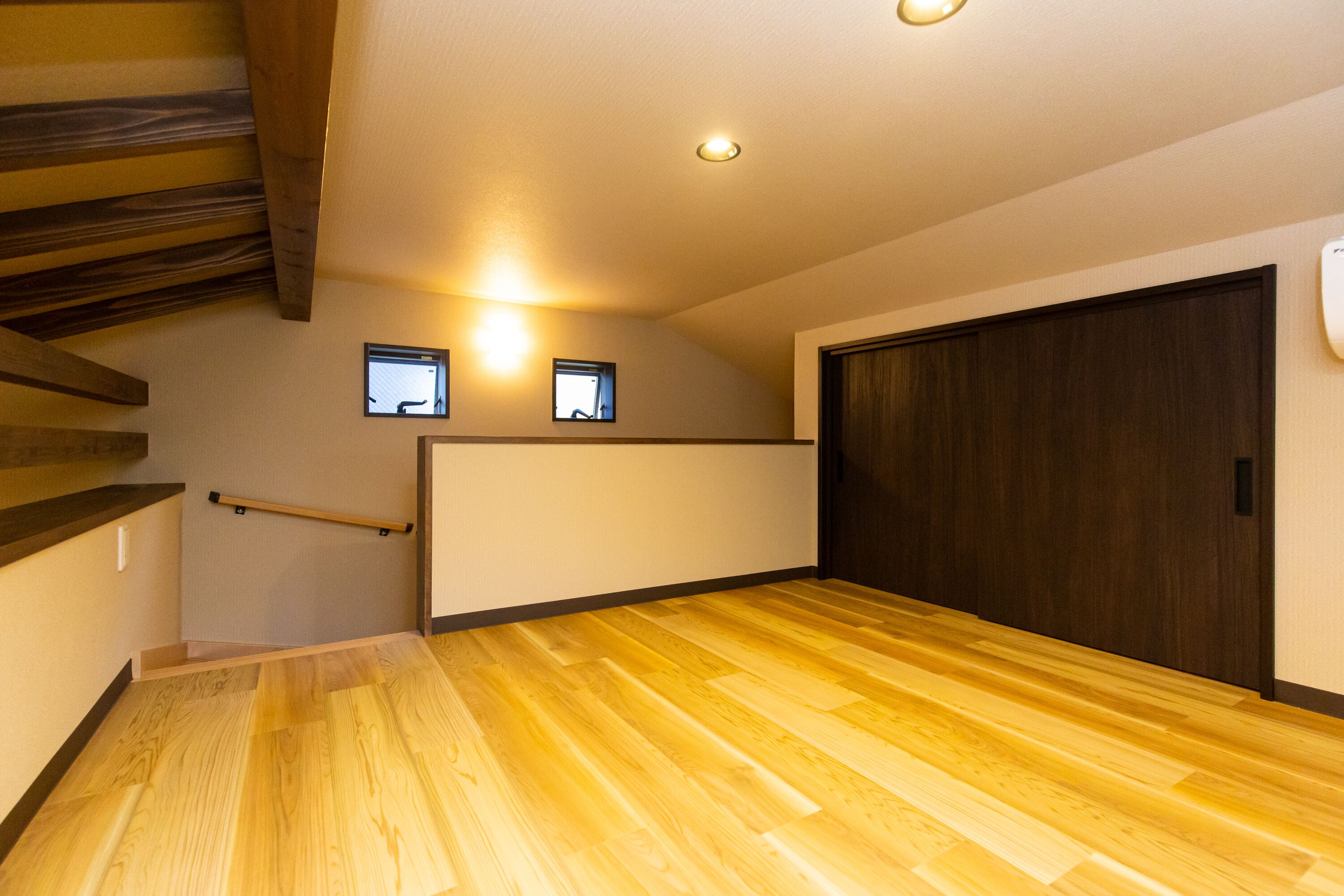 A spacious room with a wooden floor, a dark wooden door, and a small window.