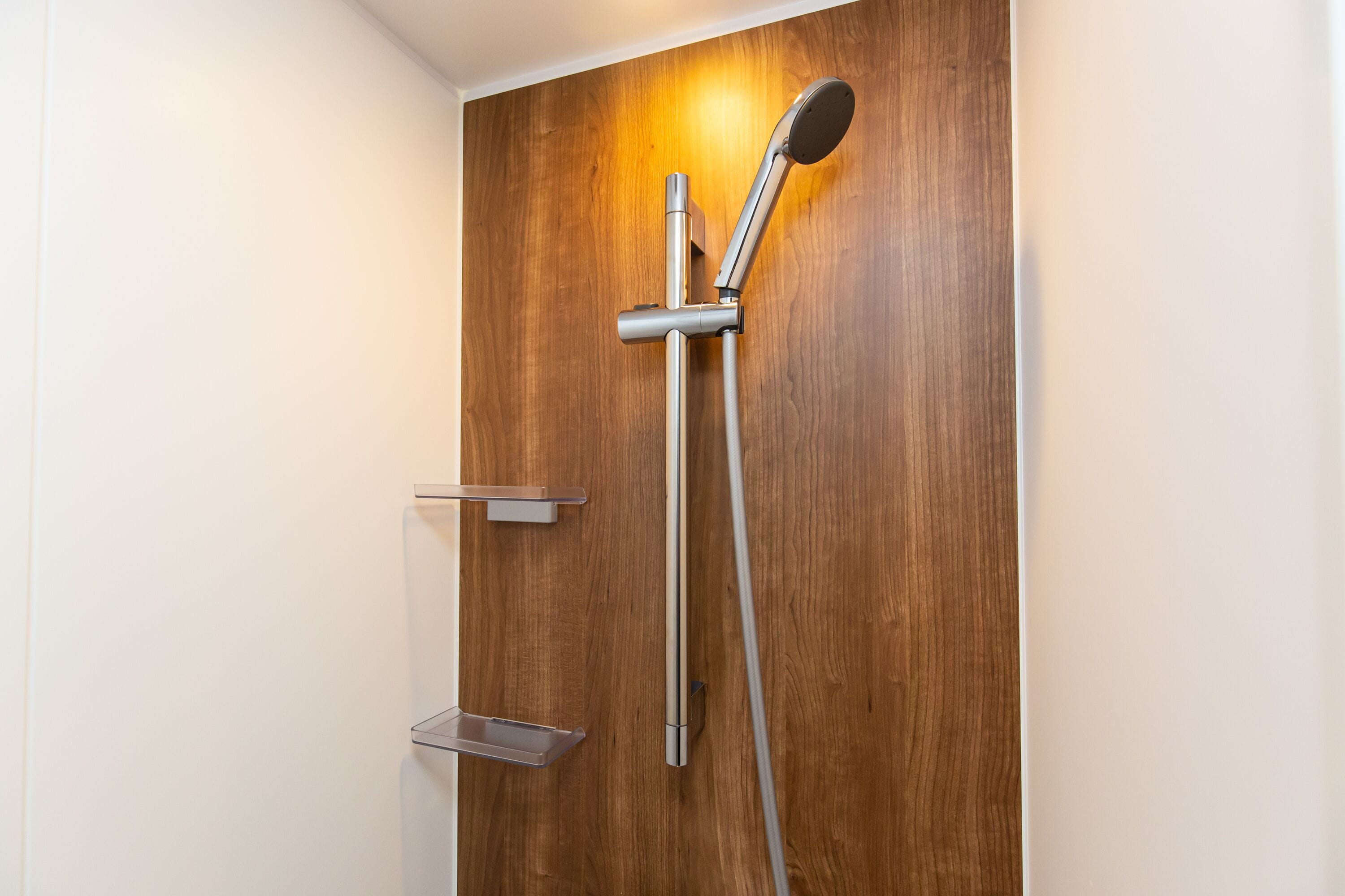 A shower with a wooden panel wall, a handheld showerhead, and a wall-mounted faucet.