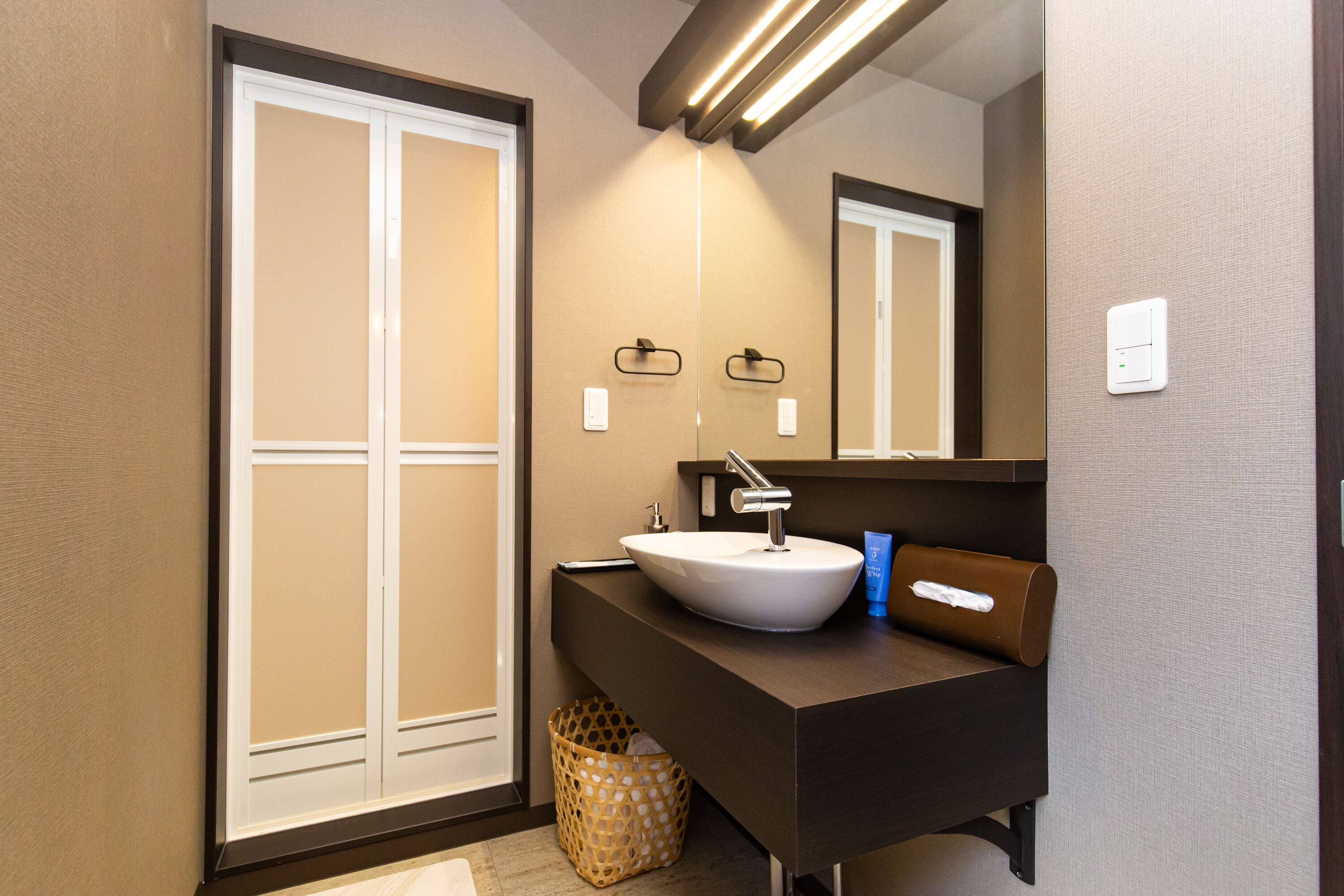 A modern bathroom with a white sink, a mirror, and a towel dispenser.