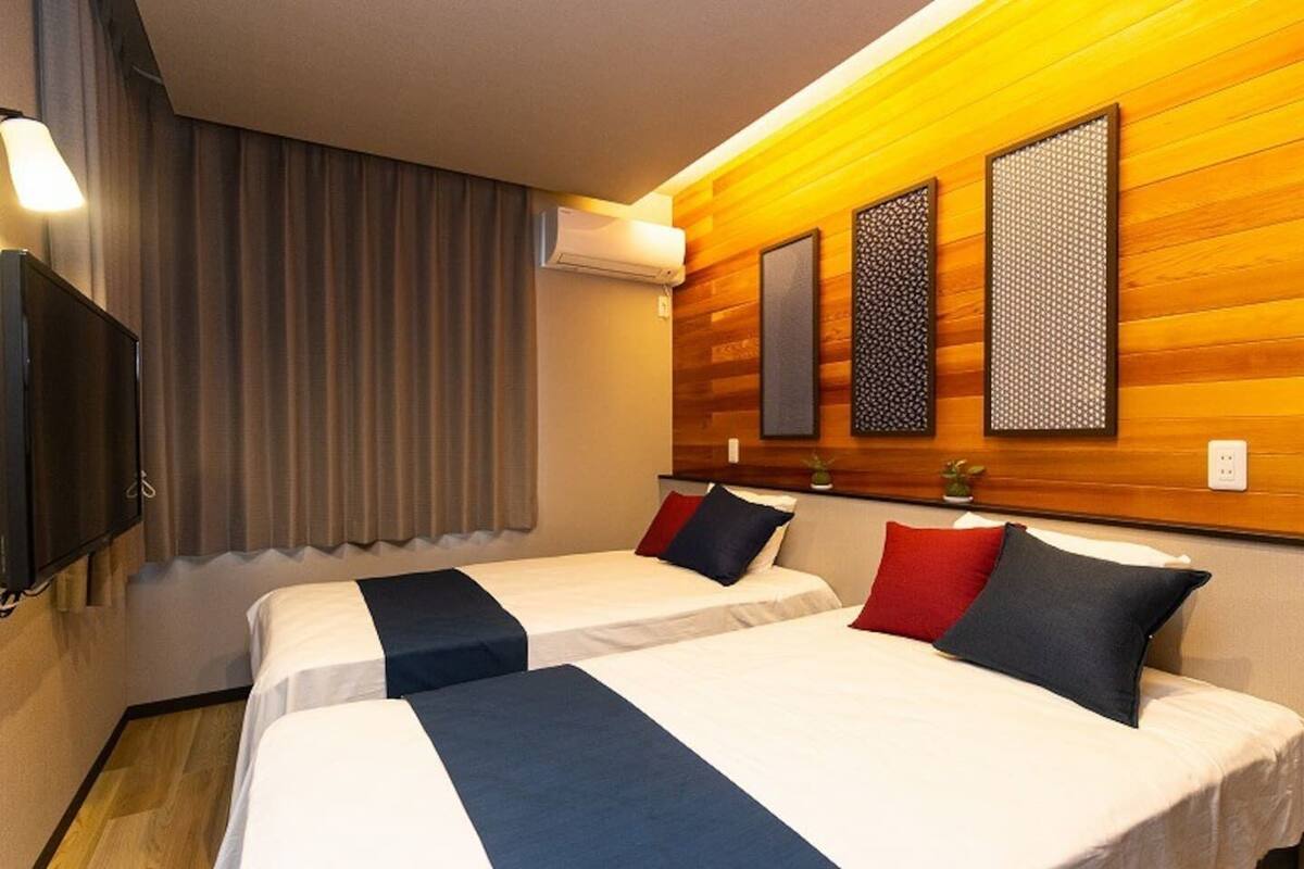 A hotel room with two beds, a flat-screen TV, and a window with curtains.