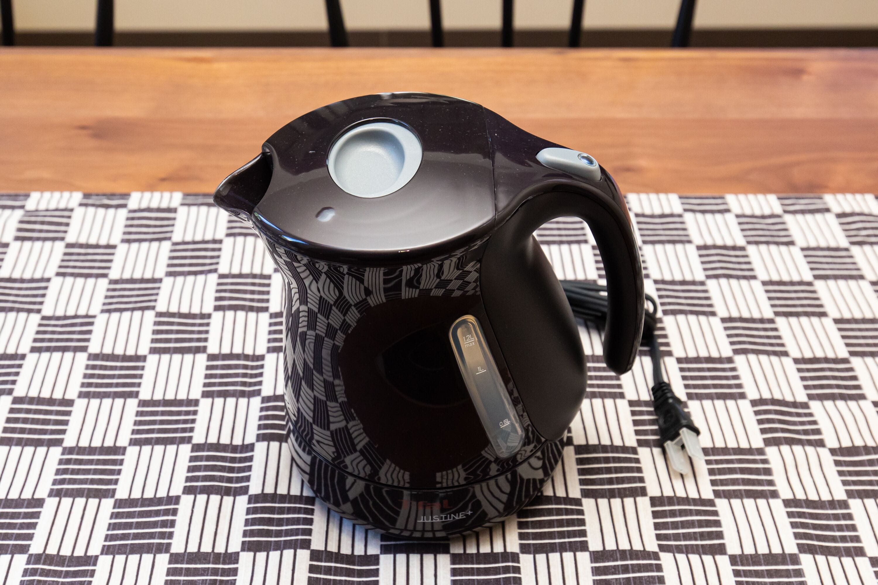 A black kettle with a transparent handle on a checkered tablecloth.