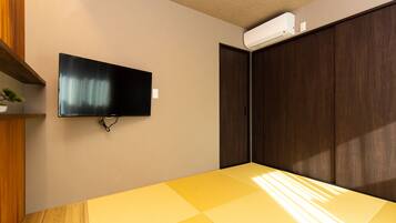 Quarto com televisão de tela plana na parede, mesa de madeira e armário com portas deslizantes.