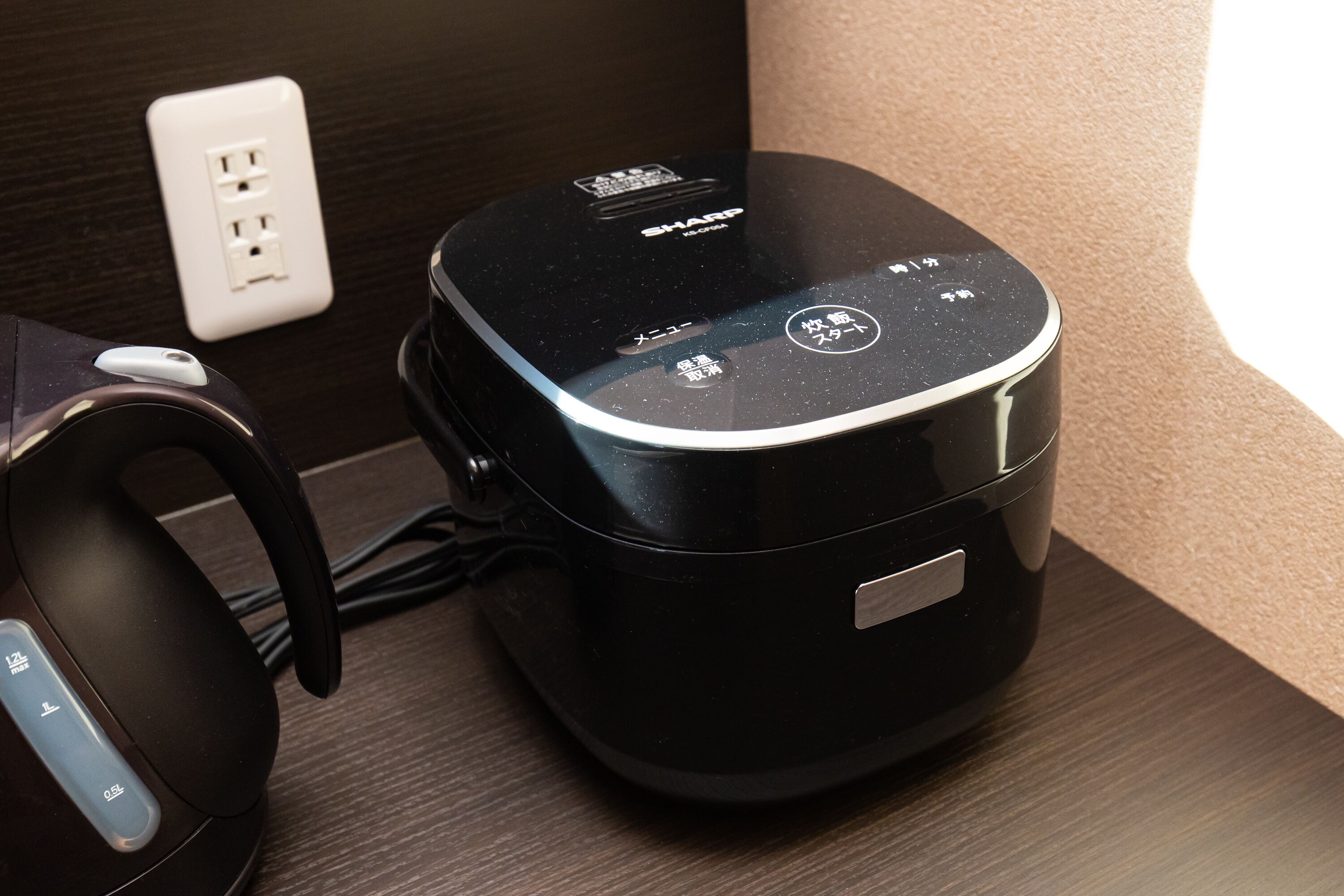 A black portable speaker with a control panel and a charging cable connected to a power outlet.