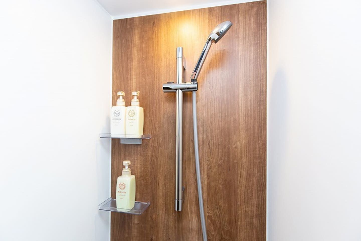 Une salle de bain avec un mur recouvert de panneaux en bois, une douche moderne et deux étagères où sont rangés les articles de toilette.