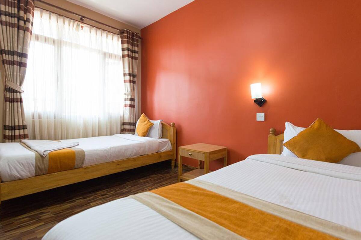 A hotel room with two single beds, a wooden headboard, a small bedside table, and a wall-mounted light.