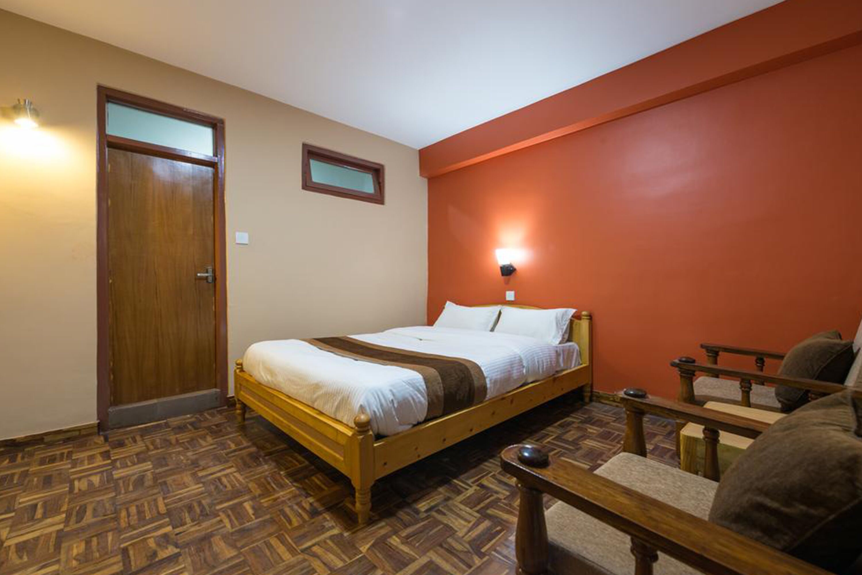 Habitación de hotel con una cama de madera, una pared decorada en rojo, una mesita y una silla.
