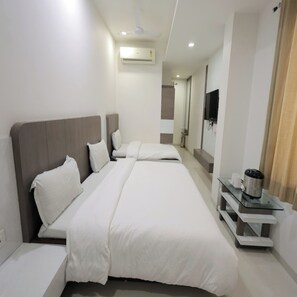 A modern hotel room with a large bed, a bedside table with a kettle, and a flat-screen TV mounted on the wall. - Hotel Grand Paradise (Vadodara)