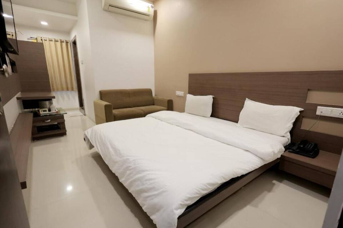 Quarto de hotel moderno com uma cama, uma cadeira, uma mesinha de cabeceira e um guarda-roupa.