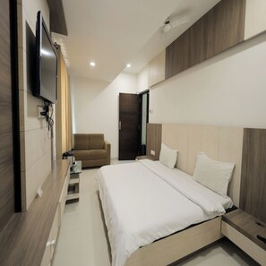 A modern bedroom with a bed, a TV mounted on the wall, and a sofa. - Hotel Grand Paradise (Vadodara)