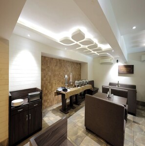 A modern dining area with a long communal table, cushioned seating, and a decorative ceiling. - Hotel Grand Paradise (Vadodara)