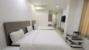 A modern hotel room with a large bed, bedside tables, a TV, and an air conditioning unit. - Hotel Grand Paradise (Vadodara)
