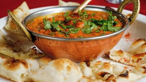 A bowl of curry with a spoon, surrounded by flatbread. - Hotel Grand Paradise (Vadodara)