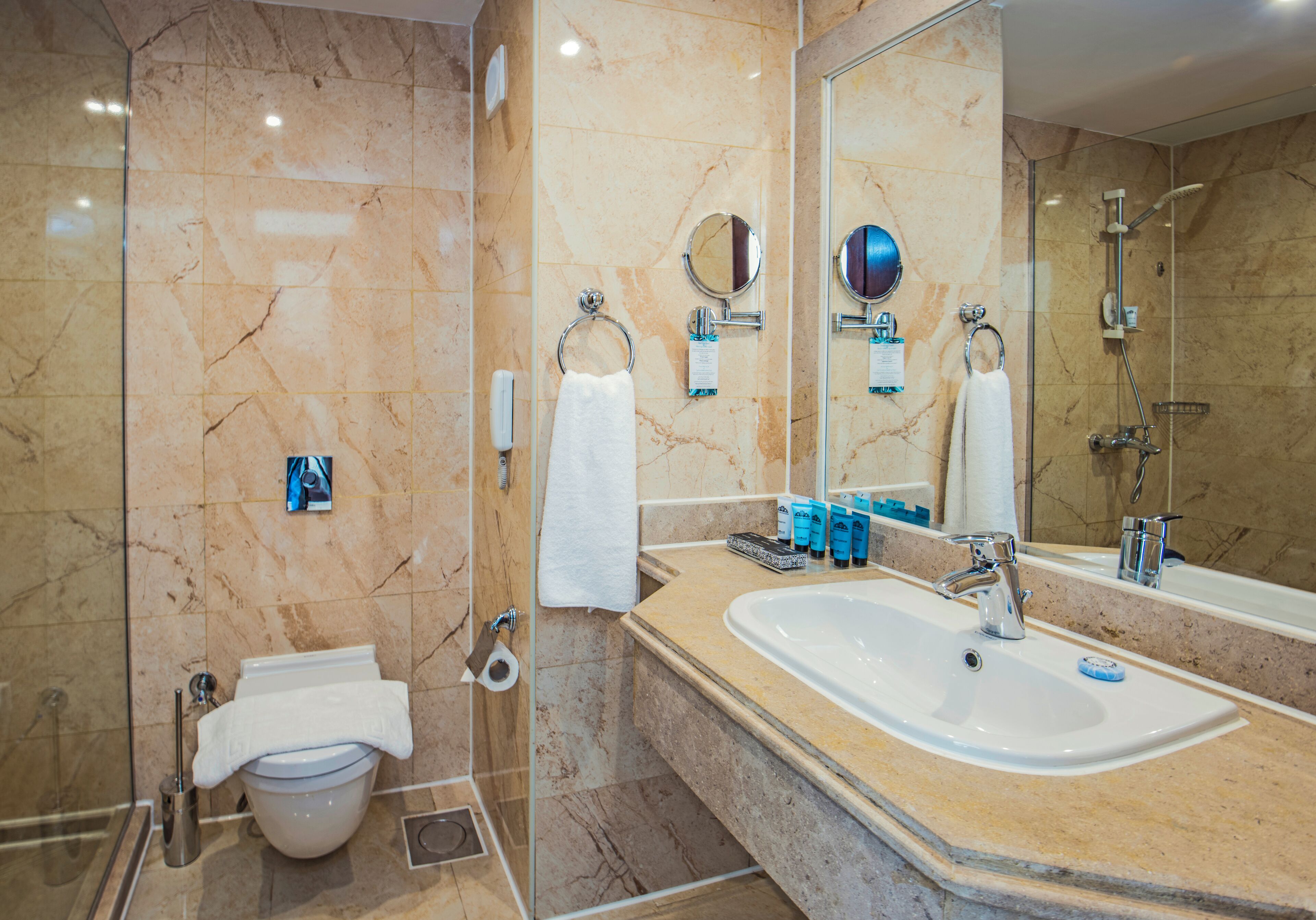 Une salle de bain moderne avec un sol en marbre, un grand lavabo, une douche en verre et un miroir.